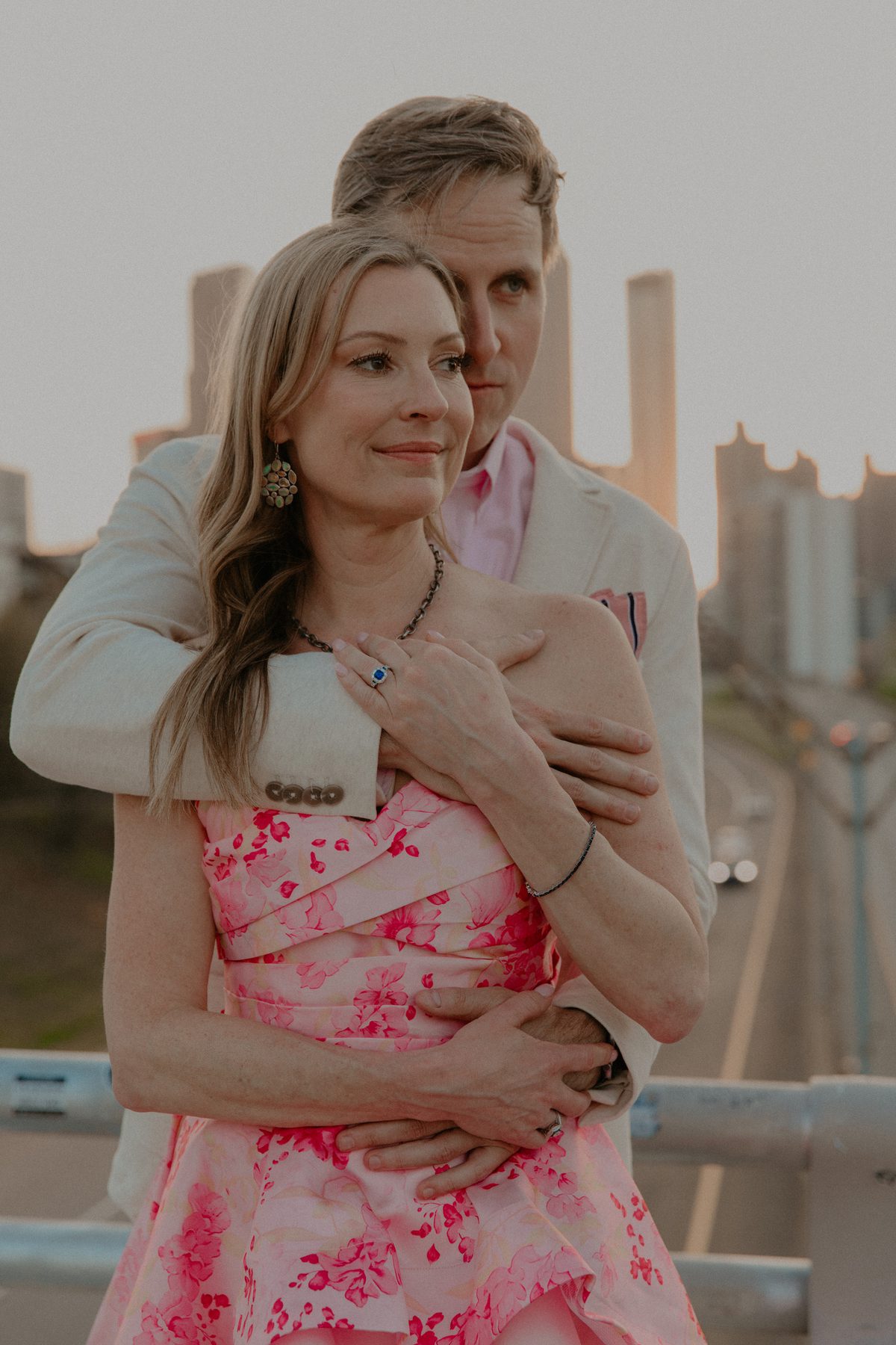 Ian embracing Kimberly from behind at sunset, her engagement ring resting on his arm