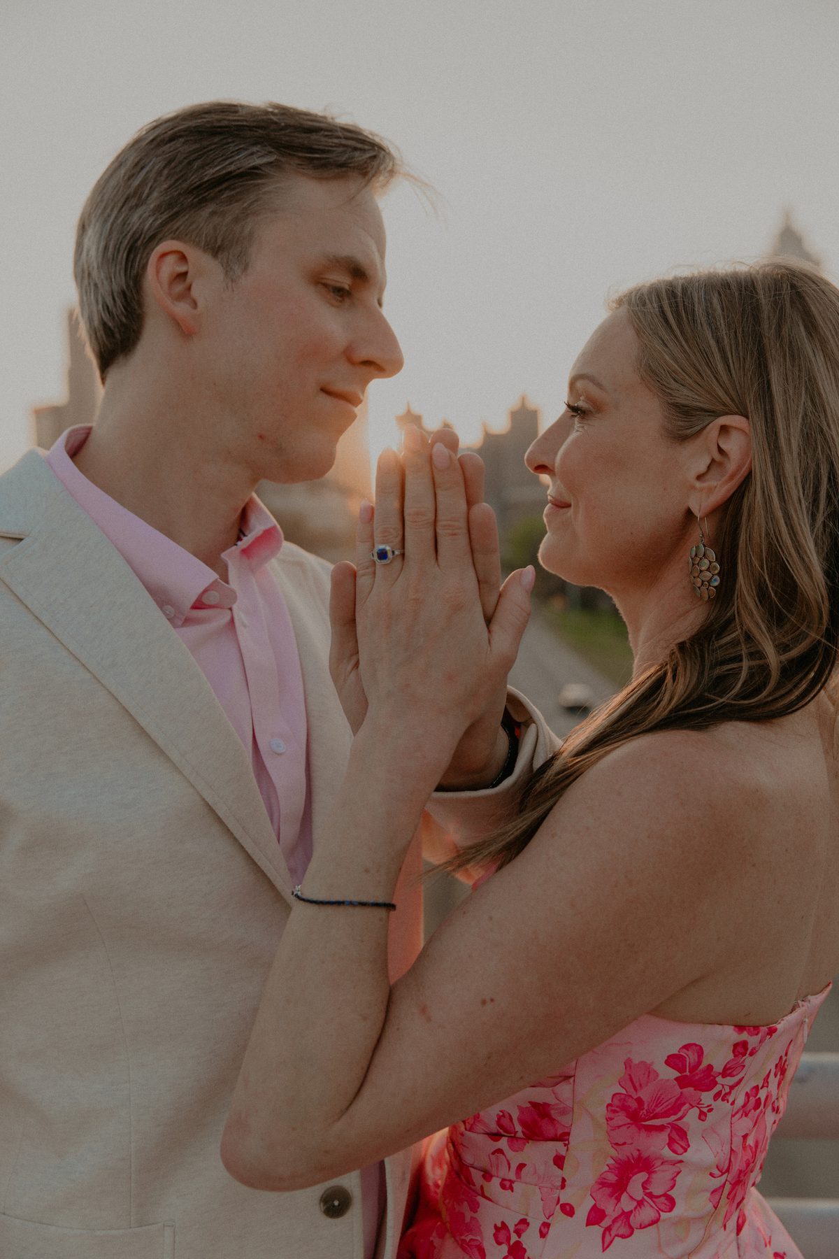 Kimberly and Ian face to face at sunset with their palms pressed together, her sapphire ring catching the light