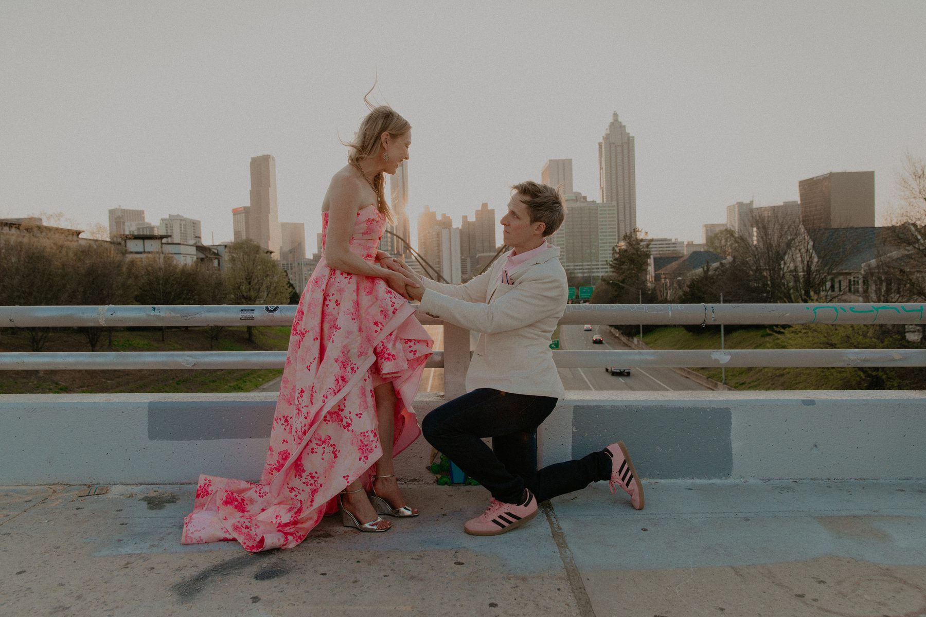Ian kneeling and holding Kimberly's hands on a bridge above the highway with the Atlanta skyline behind them