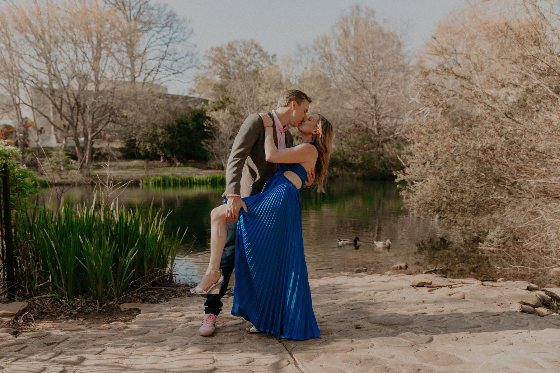 Ian dipping Kimberly for a kiss beside a pond where ducks are swimming