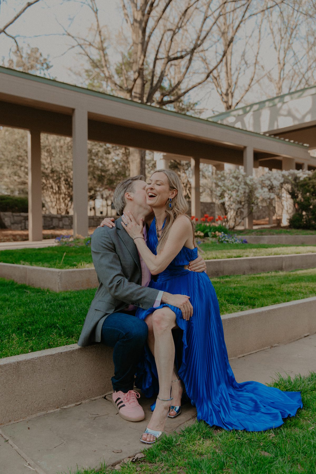 Kimberly laughing as Ian kisses her cheek while they sit on a garden ledge