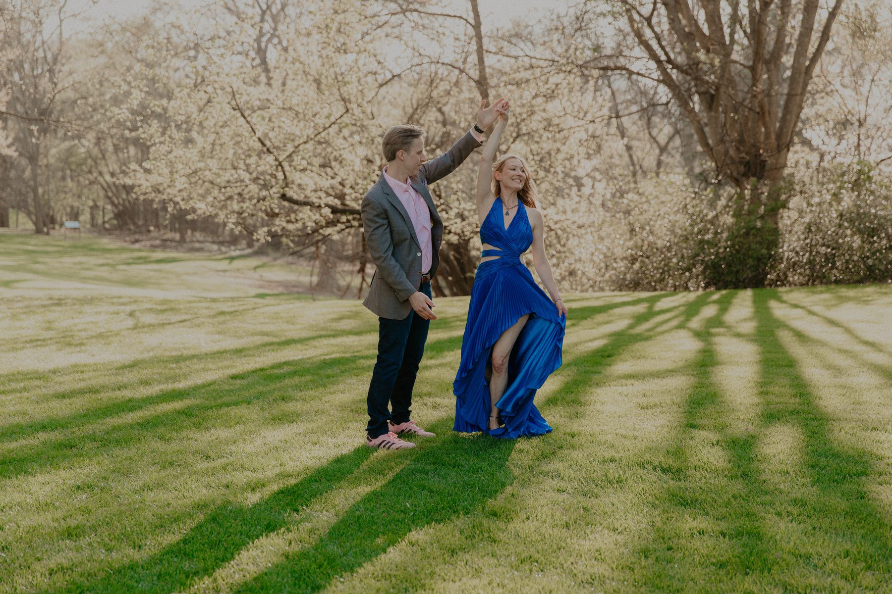 Ian twirling Kimberly in her blue gown on a sunlit lawn beneath blooming trees