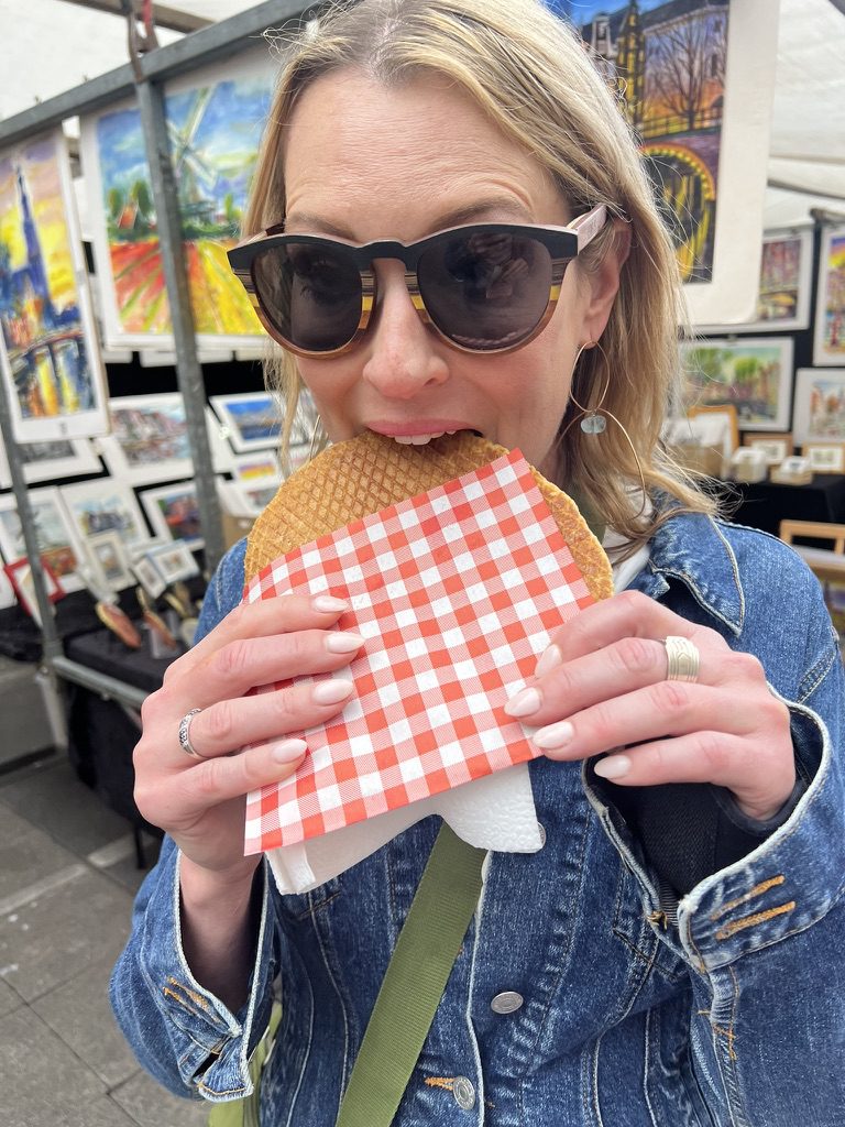 Kimberly in sunglasses taking a bite of a stroopwafel at an art market stall