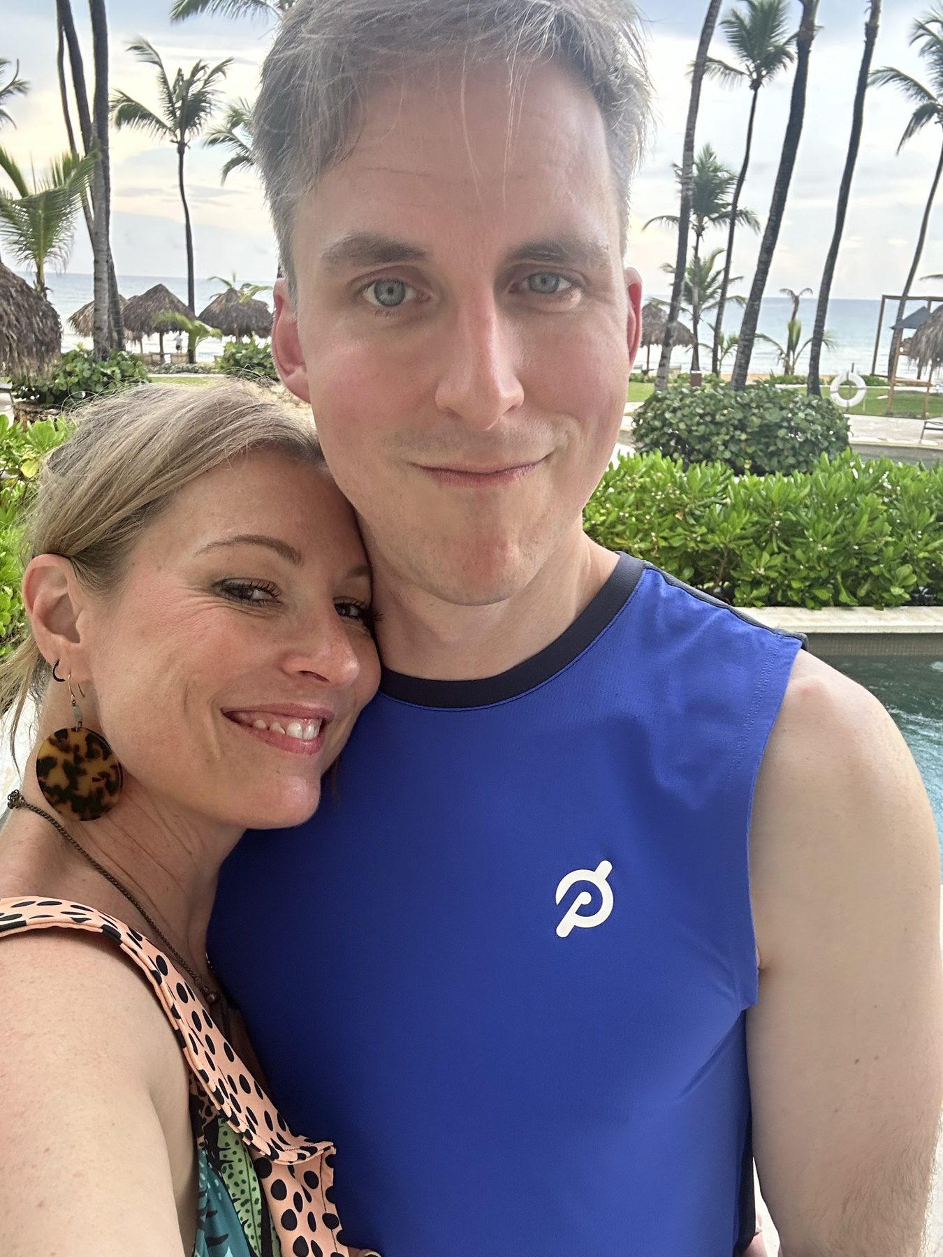 Kimberly and Ian cheek to cheek in front of palm trees and the ocean