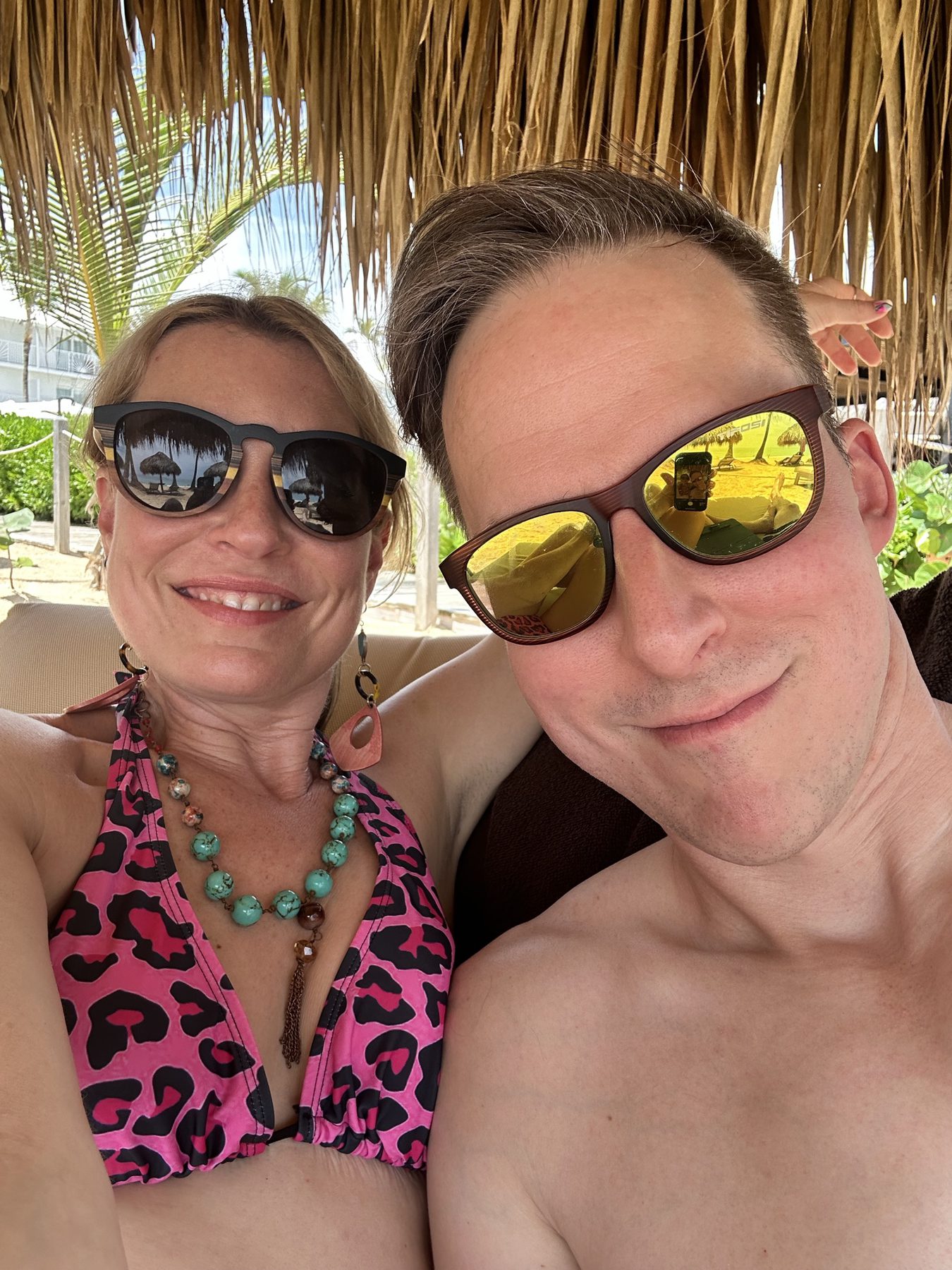 Kimberly and Ian relaxing in sunglasses under a thatched beach cabana