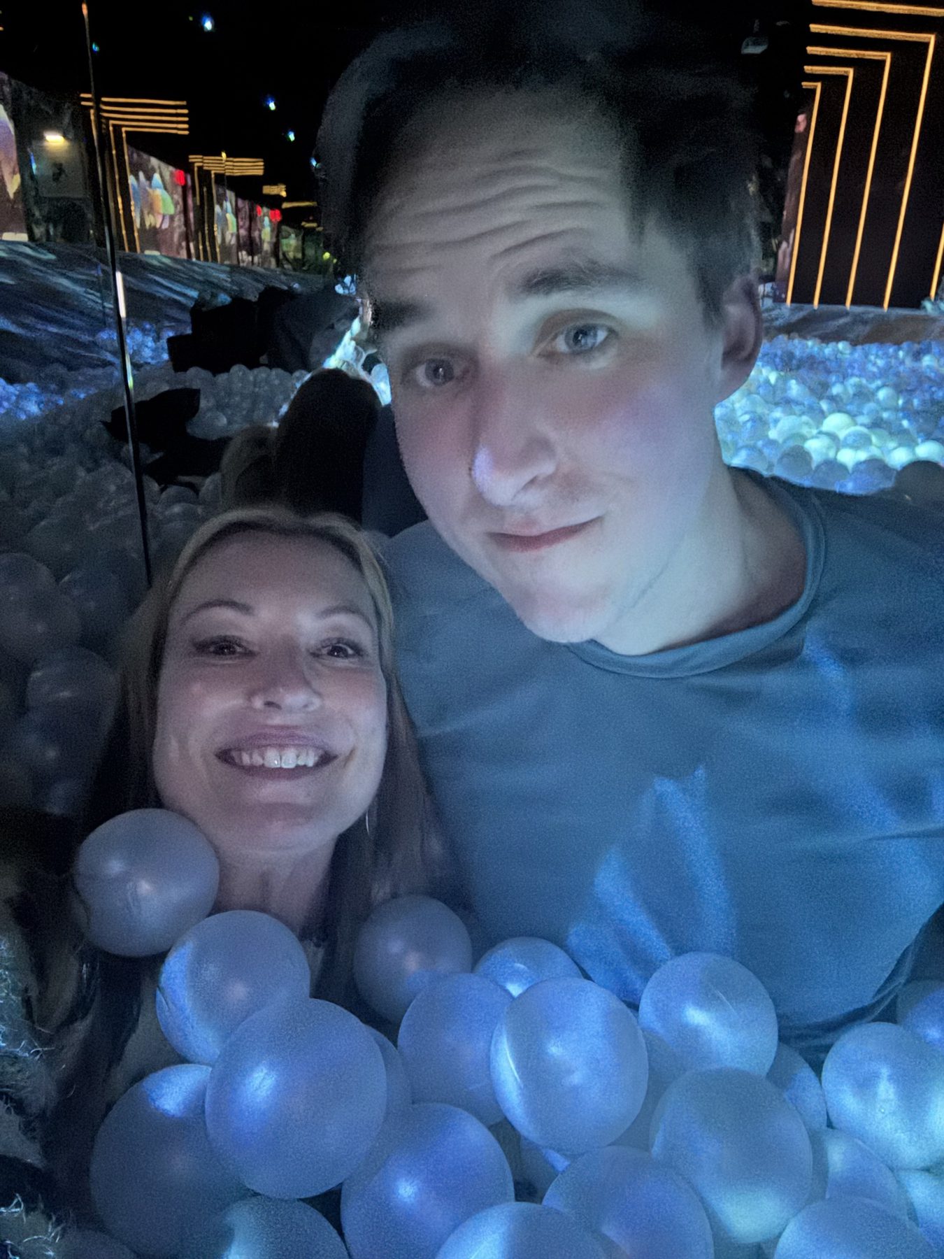 Kimberly and Ian in a glowing blue ball pit at an immersive exhibit