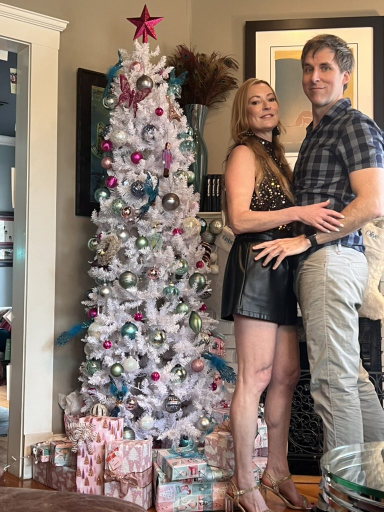 Kimberly and Ian posing arm in arm beside a white Christmas tree